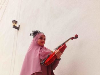 Girl holding violin while standing against wall