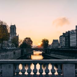 River by buildings against sky during sunset