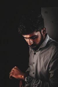 Portrait of young man looking away while standing against black background