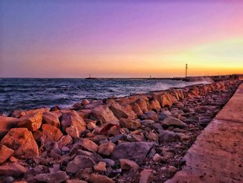 Rocks by sea against sky during sunset