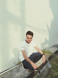 Portrait of young man sitting against wall