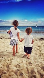 Rear view of boy and girl walking on beach