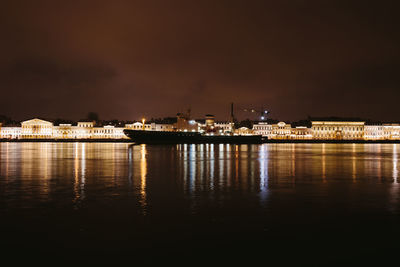 Illuminated city by sea against sky at night