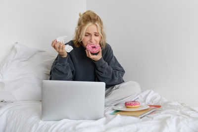 Portrait of young woman using phone while sitting on bed at home