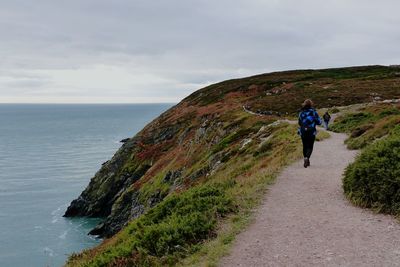 Rear view of woman walking on mountain road by sea against sky