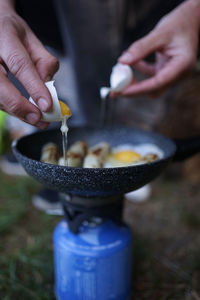 Preparing egg sausage on a frying pan with a camping gas stove at outdoor camp.