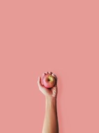 Cropped hand holding apple against coral background
