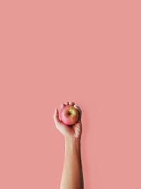 Close-up of hand holding apple against pink background