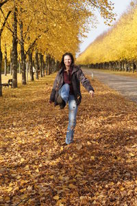 Young woman kicking autumn leaves on field by trees