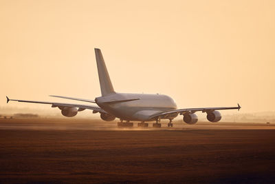 Huge airplane taking off from airport runway at golden sunset.
