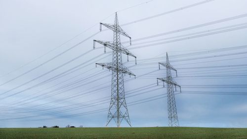 Low angle view of electricity pylon on field against sky