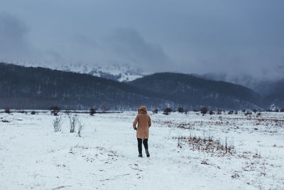 Rear view of woman standing on snow covered field