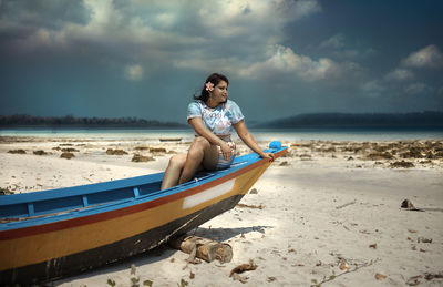 Young man sitting on shore at beach against sky