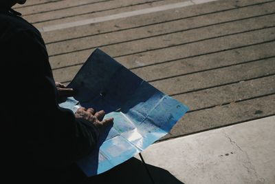 Midsection of man reading map in city during sunny day