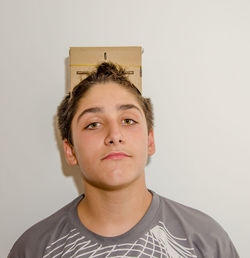 Portrait of sad boy with cardboard box while standing against wall