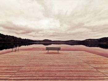 Empty bench by lake against sky