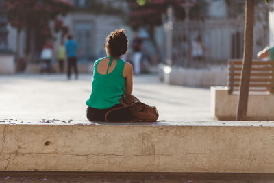 Rear view of woman sitting on retaining wall