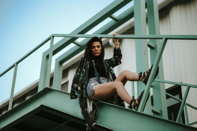 Young woman sitting on staircase against building