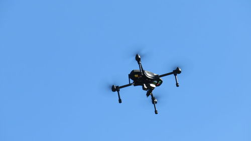 Low angle view of drone flying against clear blue sky