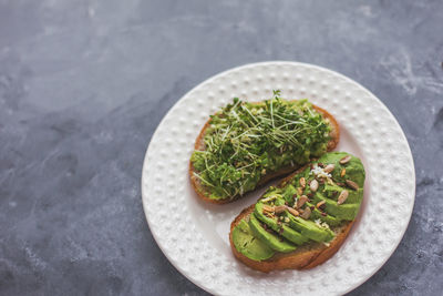 Vegan avocado sandwich with microgreens on a white plate on a gray background