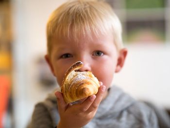 Portrait of boy eating croissant at home