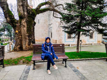 Full length portrait of teenage girl sitting on bench against building