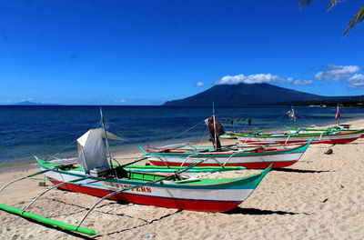 Boats moored on beach against blue sky