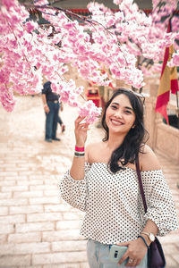 Portrait of smiling woman standing by flowering tree on footpath