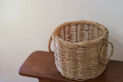 Brown wicker basket on a wooden table with cement wall behind