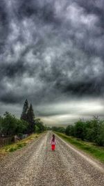 Road amidst field against storm clouds