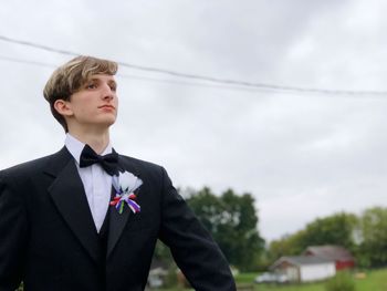Low angle view of young man looking away while standing against cloudy sky