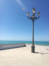 Street light by sea against clear blue sky