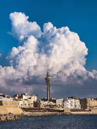 Communications tower in city against cloudy sky