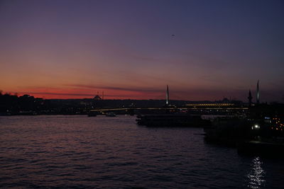 Illuminated city at waterfront during sunset