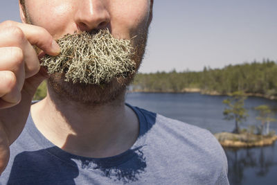 Close-up of young man holding lichen on mustache