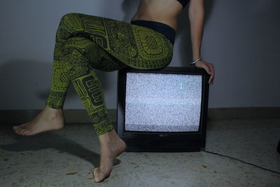 Low section of woman sitting on television set at home