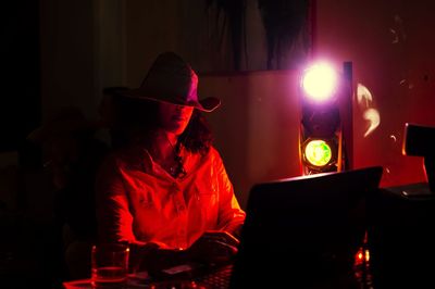 Woman wearing hat using laptop in illuminated house