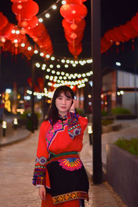 Young woman looking away while standing against illuminated lights at night