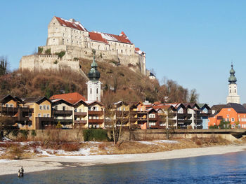 Buildings by river in town against clear sky