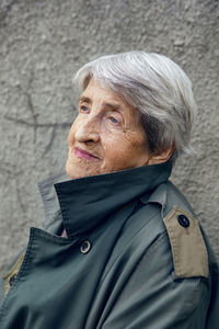 Portrait of an old siniors grandmother of 90 with gray hair stands against a gray wall on the street