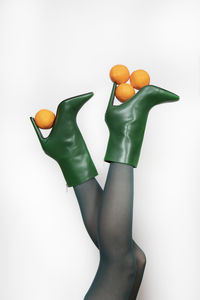 Woman in green stilettos balancing oranges against white background