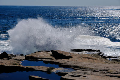 Waves splashing on rocks at shore against sky