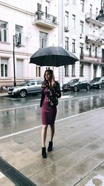 Full length of woman standing on wet street in rainy season