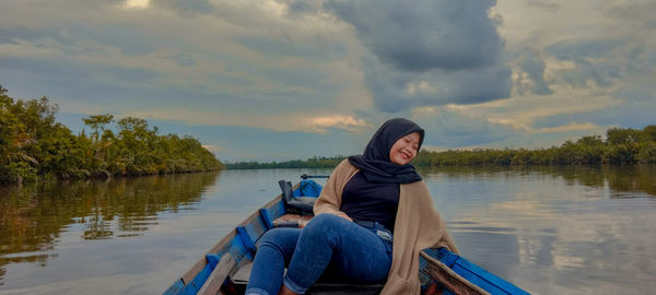 Woman sitting by lake against sky