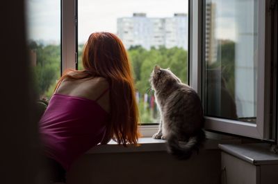 Rear view of woman by cat looking through window