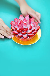 Cropped hand of person holding strawberry cake on table