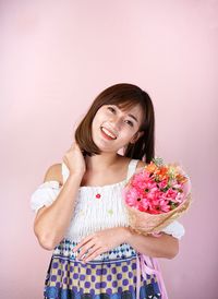 Portrait of smiling woman standing against pink wall