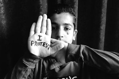 Portrait of teenage boy with i protest text on palm against wall