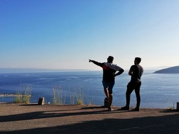 Friends standing on sea shore against clear sky