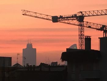 Silhouette crane by building against sky during sunset